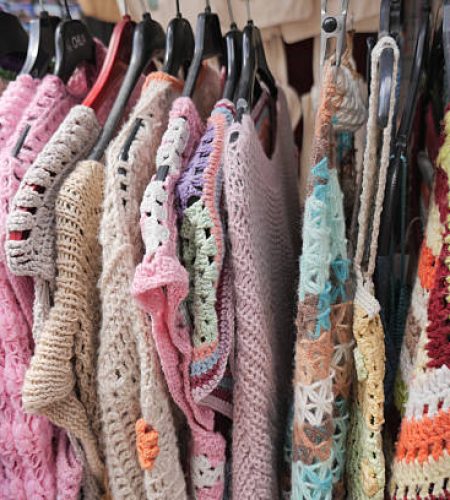 Various crochet garments are showcased on hangers inside a boutique.